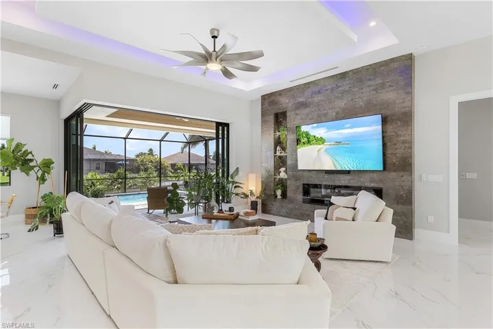 Tiled living room with ceiling fan, a tray ceiling, tile walls, and a fireplace