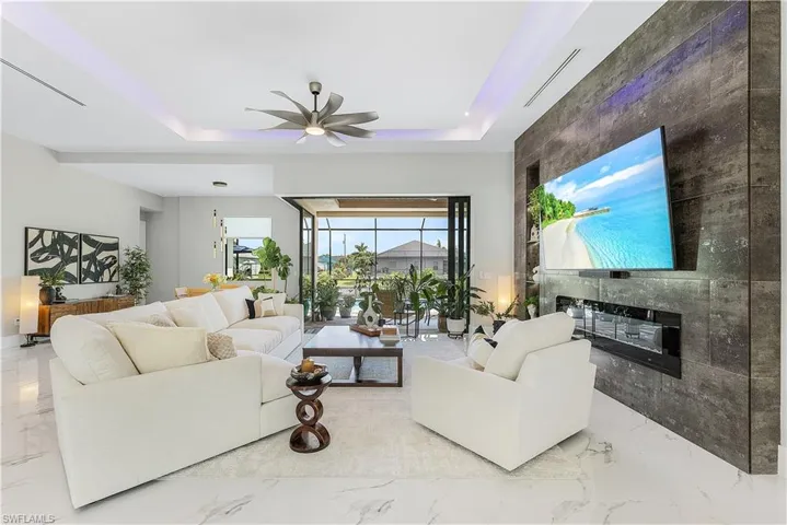 Living room featuring a tray ceiling, ceiling fan, light tile patterned floors, and a premium fireplace