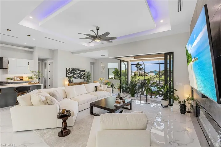 Living room with ceiling fan, a raised ceiling, and light tile patterned floors