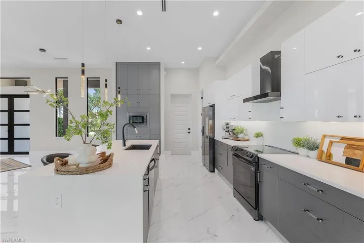 Kitchen with sink, decorative light fixtures, a kitchen island with sink, stainless steel appliances, and wall chimney range hood