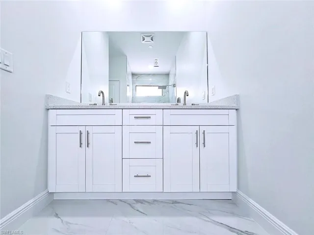 Bathroom with marble finish floor, baseboards, a sink, and double vanity