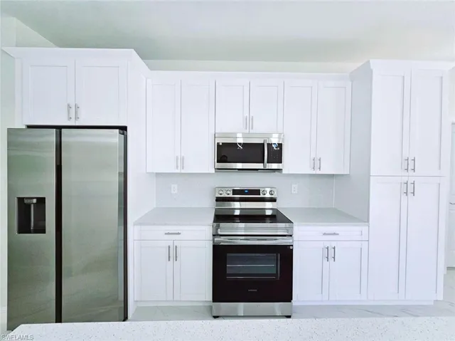 Kitchen with light countertops, appliances with stainless steel finishes, and white cabinetry