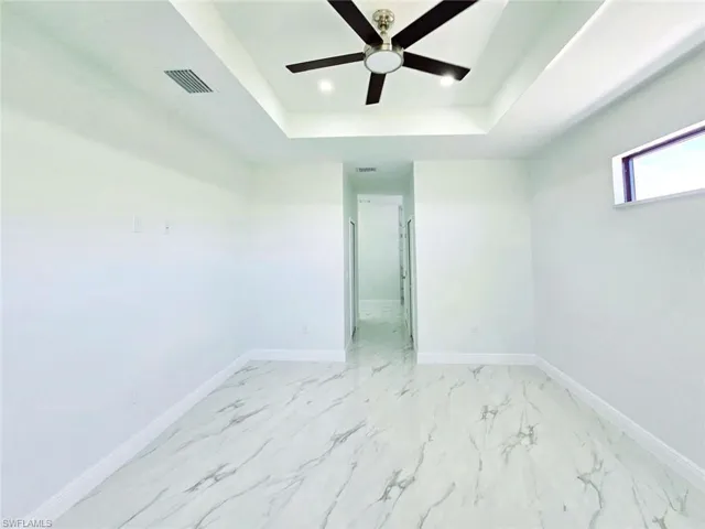 Spare room featuring a tray ceiling, visible vents, baseboards, recessed lighting, and a ceiling fan