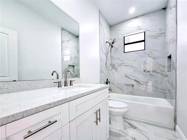 Full bathroom featuring toilet, baseboards, marble finish floor, vanity, and shower / tub combination