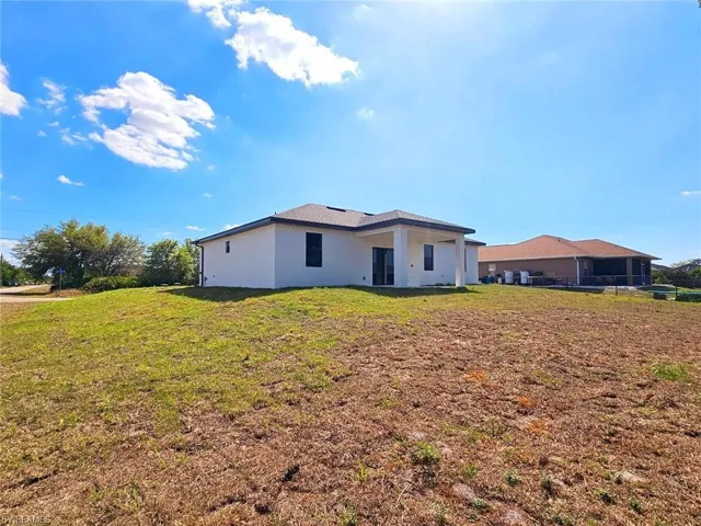 Rear view of property featuring a lawn and stucco siding