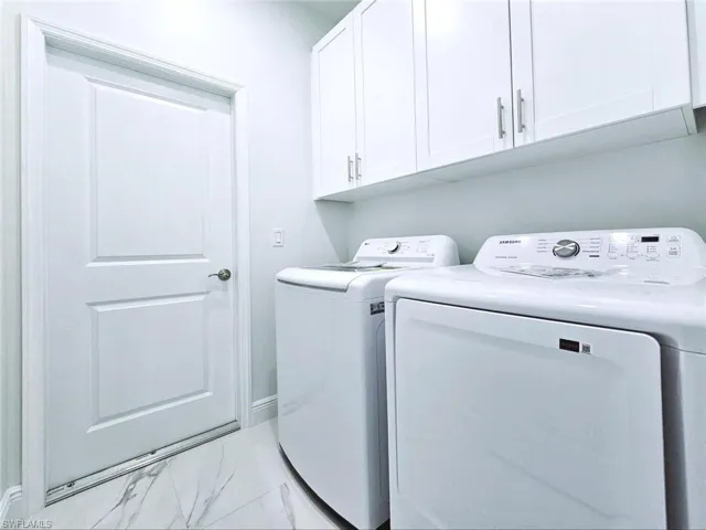 Clothes washing area with cabinet space, marble finish floor, and washer and dryer