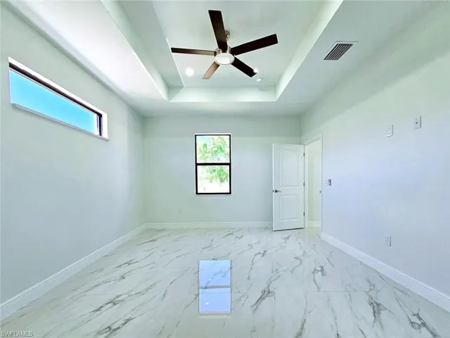 Spare room with baseboards, visible vents, a raised ceiling, and a healthy amount of sunlight