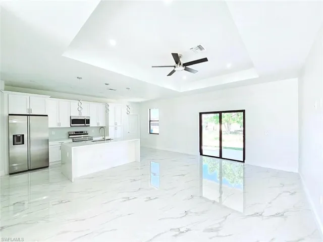 Unfurnished living room featuring baseboards, a ceiling fan, visible vents, and a raised ceiling