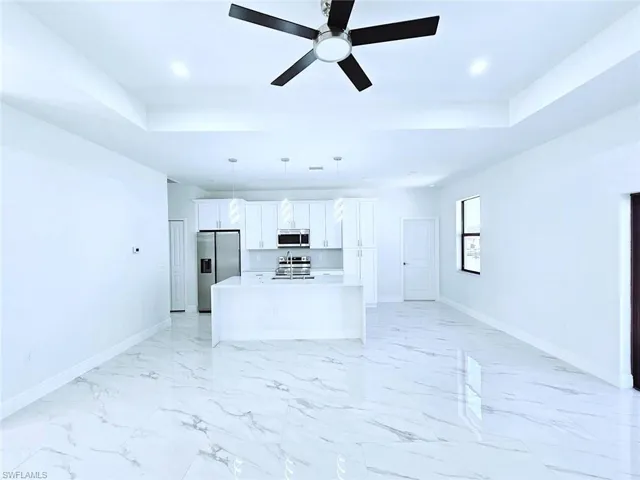 Unfurnished living room with baseboards, a tray ceiling, recessed lighting, and ceiling fan