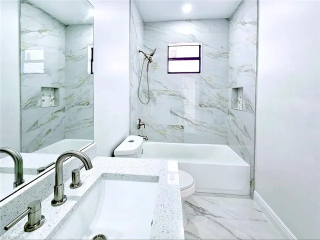 Bathroom with washtub / shower combination, marble finish floor, toilet, vanity, and baseboards