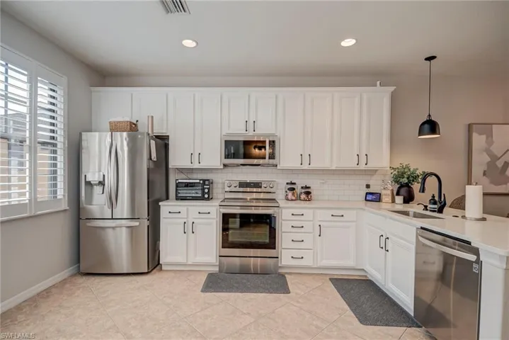 Kitchen featuring stainless steel appliances, white cabinetry, hanging light fixtures, decorative backsplash, and recessed lighting
