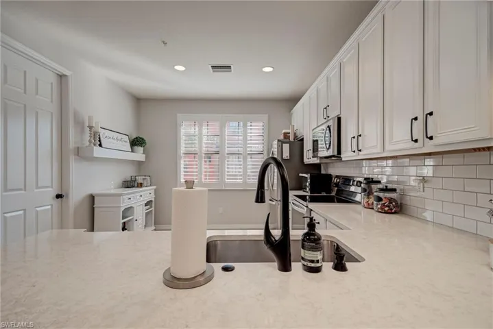 Kitchen featuring stainless steel appliances, white cabinets, tasteful backsplash, light stone countertops, and recessed lighting