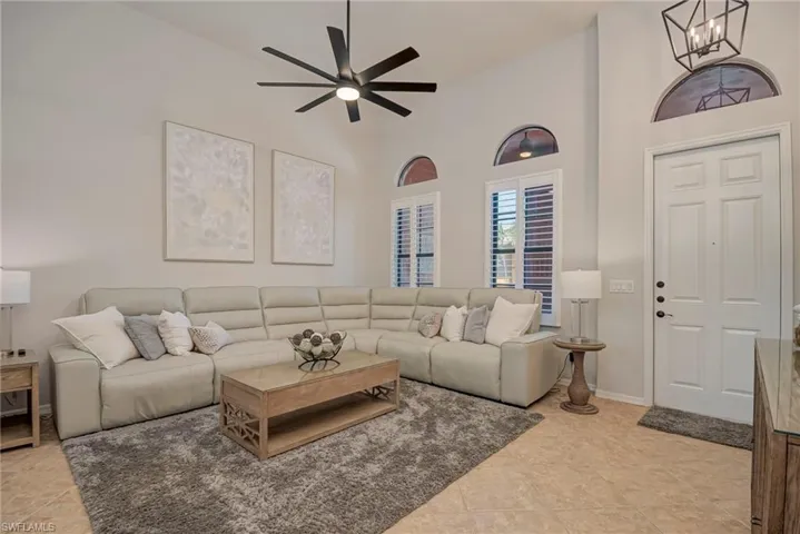 Living area with a towering ceiling, light tile patterned floors, and ceiling fan