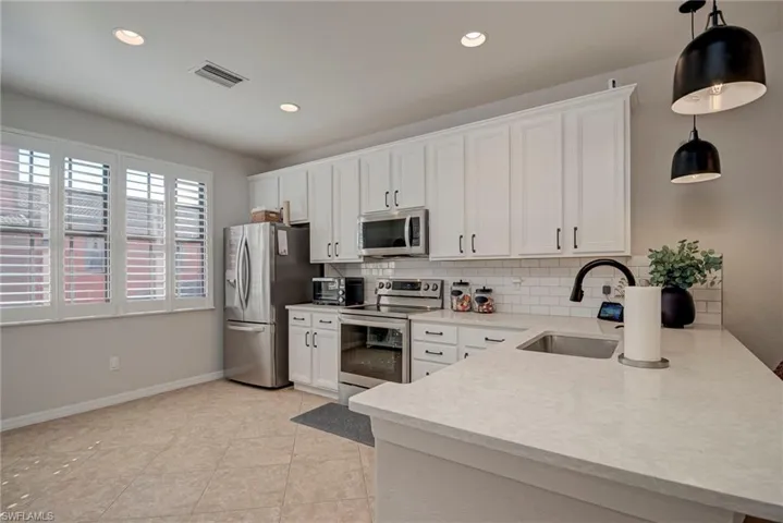 Kitchen featuring appliances with stainless steel finishes, backsplash, white cabinetry, decorative light fixtures, and recessed lighting