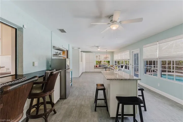 Kitchen with freestanding refrigerator, ceiling fan, a kitchen bar, a kitchen island, and light stone counters