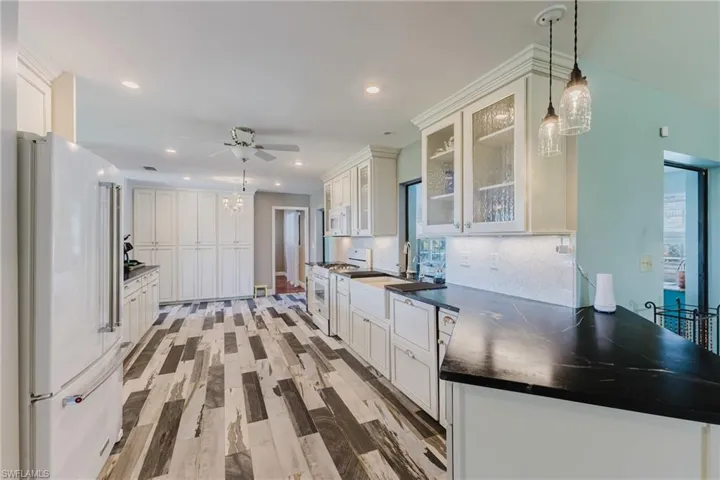 Kitchen featuring white appliances, dark countertops, backsplash, ceiling fan, and light wood-type flooring