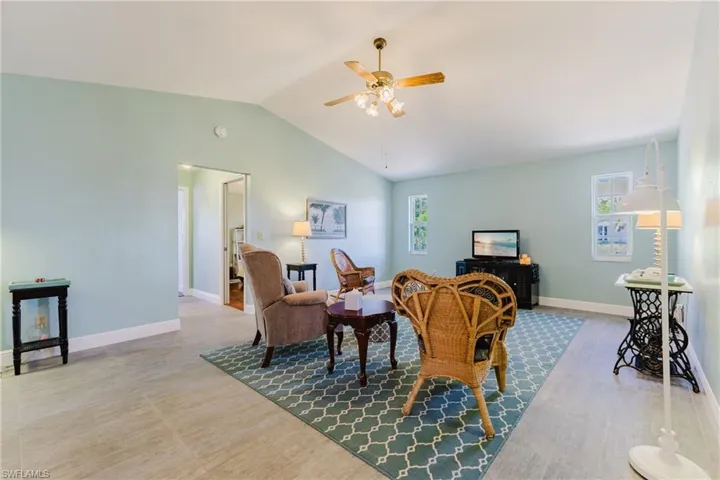 Living room featuring vaulted ceiling, a ceiling fan, baseboards, and wood finished floors