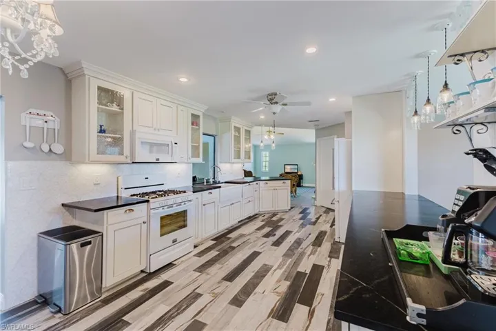 Kitchen featuring white appliances, dark countertops, a peninsula, ceiling fan, and pendant lighting
