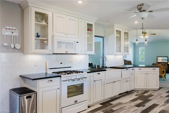 Kitchen featuring white appliances, a ceiling fan, dark countertops, backsplash, and white cabinetry