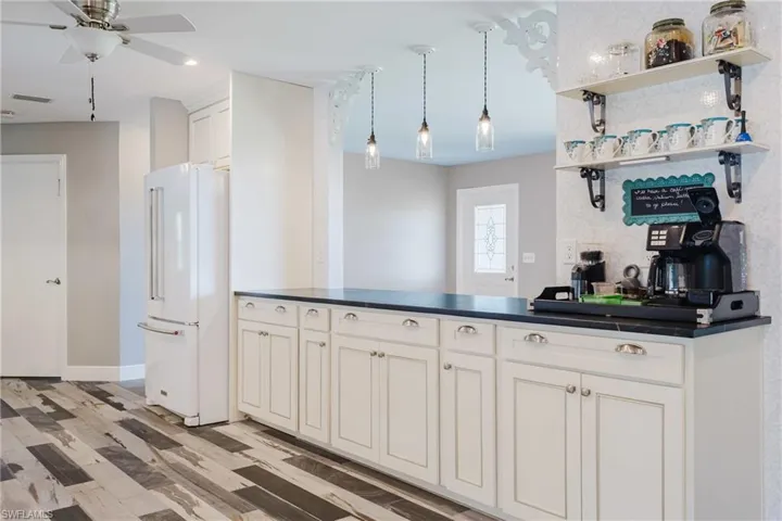 Kitchen featuring freestanding refrigerator, dark countertops, a ceiling fan, light wood finished floors, and a peninsula