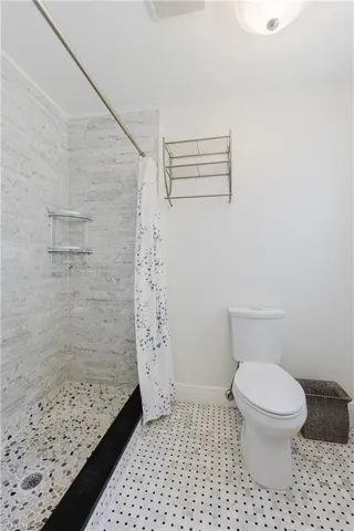 Full bath featuring toilet, baseboards, a tile shower, and tile patterned flooring