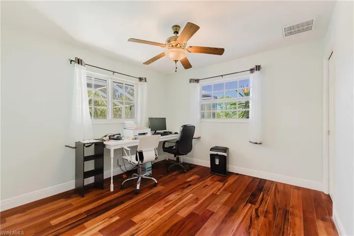 Home office with dark wood finished floors, healthy amount of natural light, a ceiling fan, and baseboards