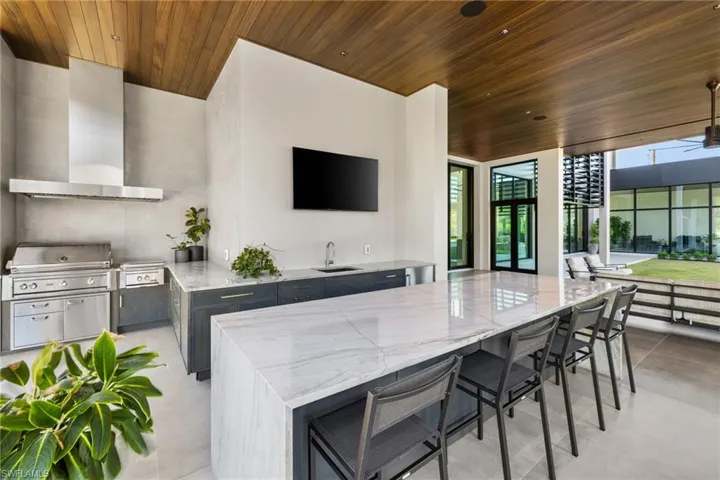 Kitchen featuring light stone countertops, a kitchen island, wooden ceiling, and wall chimney range hood
