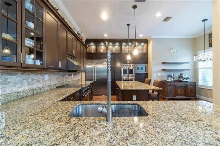Kitchen with decorative backsplash, hanging light fixtures, built in appliances, and light stone counters