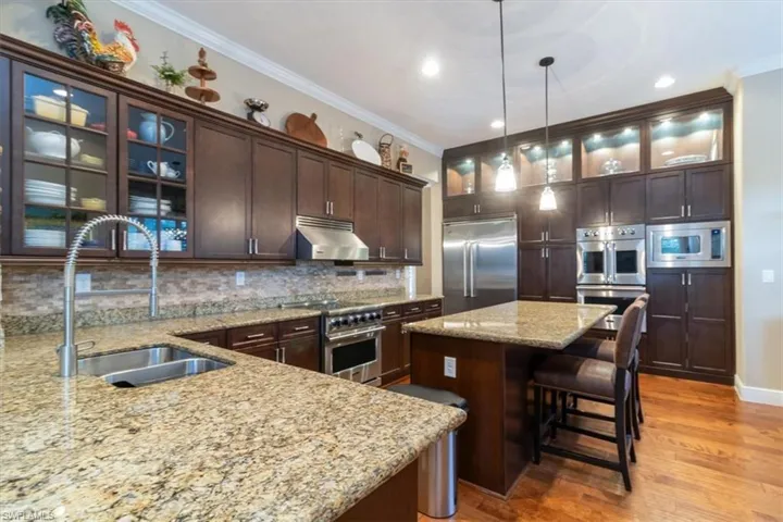 Kitchen featuring decorative backsplash, light wood-type flooring, built in appliances, dark brown cabinetry, and sink