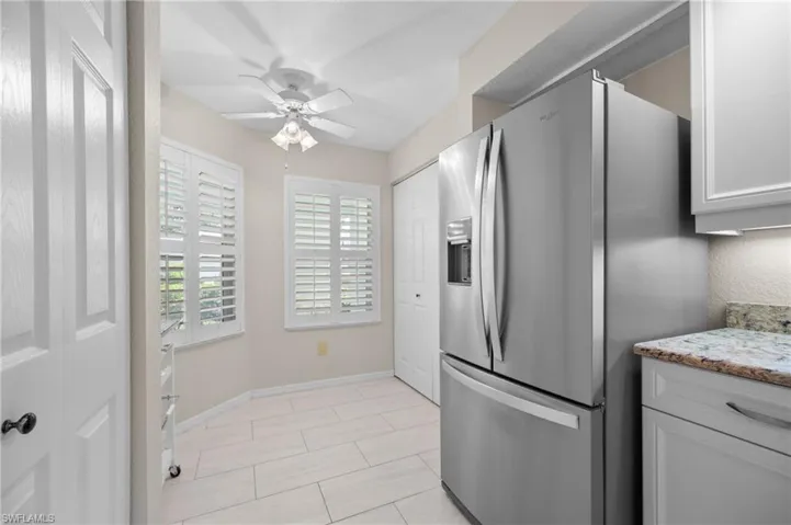 Kitchen area featuring stainless steel French door refrigerator, white cabinetry, light-toned countertop, and tiled flooring