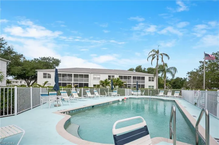 Community swimming pool with a light blue deck, surrounded by white fencing and mature landscaping