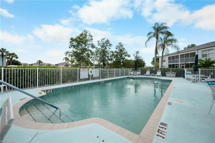 Community swimming pool featuring a curved entry with built-in steps, a surrounding white picket fence, and multiple poolside seating areas