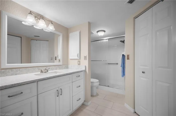 Spacious bathroom featuring a double vanity with white cabinetry and a light-toned countertop, a frameless glass-enclosed shower, and light-toned tile flooring