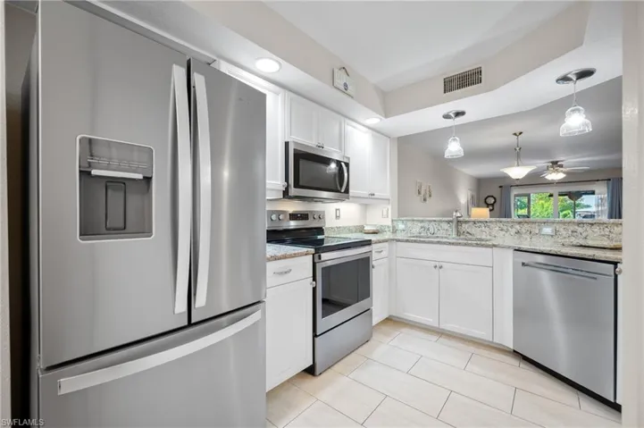 Kitchen featuring stainless steel appliances, white cabinetry, recessed lighting, and a pass-through window with pendant lighting