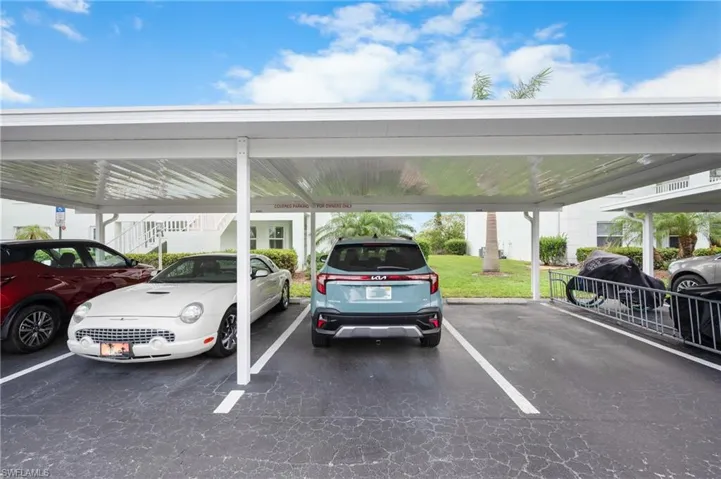 Covered parking structure with multiple designated spaces, featuring a clear corrugated roof and white support columns