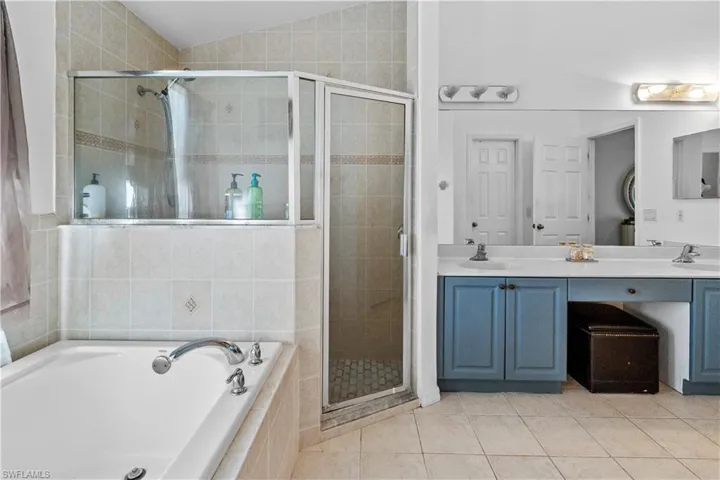 Bathroom featuring double vanity, a bath, a stall shower, light tile patterned flooring, and vaulted ceiling