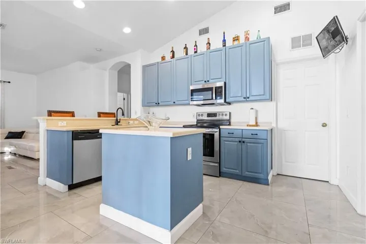 Kitchen featuring stainless steel appliances, arched walkways, lofted ceiling, light countertops, and blue cabinets