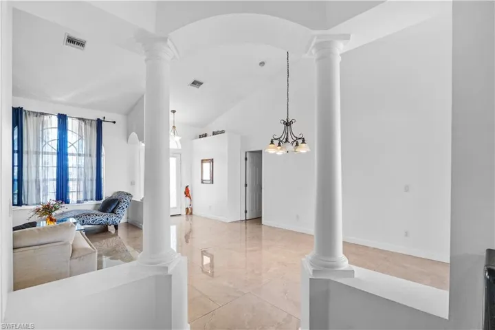 Living area with ornate columns, arched walkways, lofted ceiling, and suspended lighting