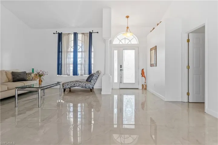 Foyer featuring decorative columns, light marble finish floors, and lofted ceiling