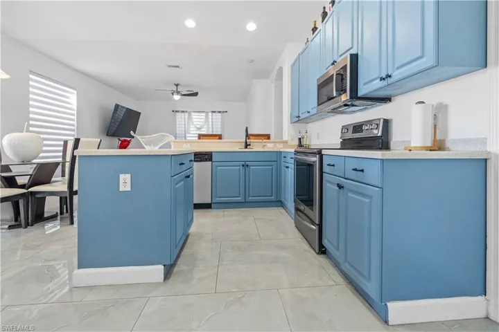 Kitchen with blue cabinetry, a peninsula, stainless steel appliances, ceiling fan, and recessed lighting