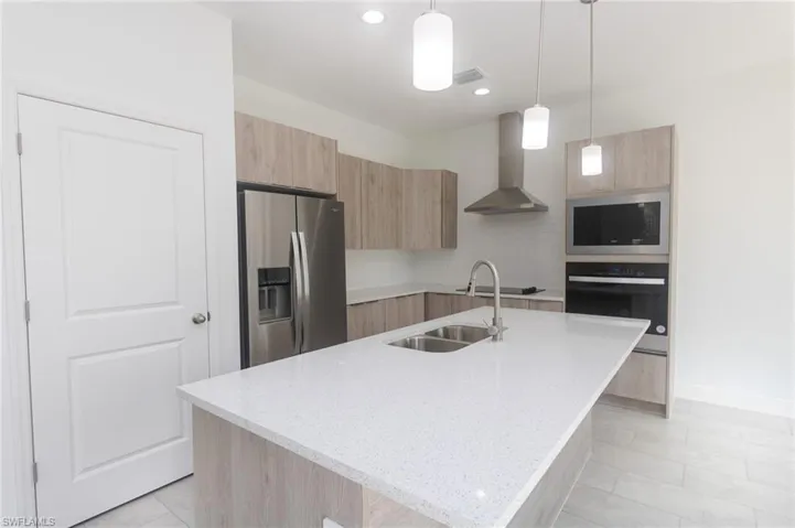 Kitchen with wall chimney range hood, modern cabinets, appliances with stainless steel finishes, and light brown cabinetry