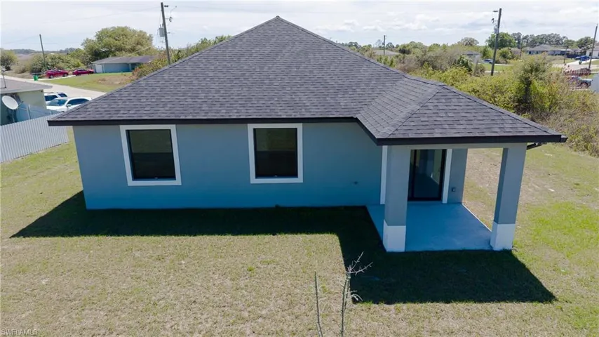 Back of house featuring roof with shingles, a lawn, a patio, and stucco siding
