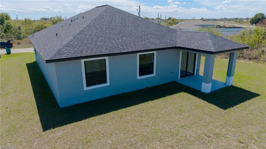 Rear view of house with a lawn, a shingled roof, a patio, and stucco siding