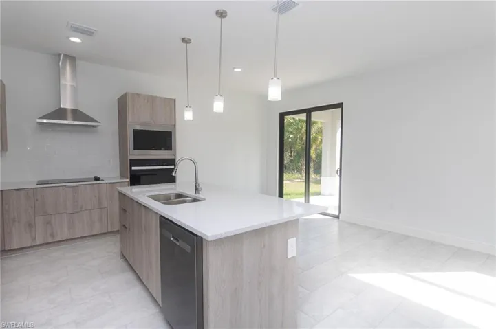 Kitchen with wall chimney range hood, modern cabinets, appliances with stainless steel finishes, and light brown cabinetry