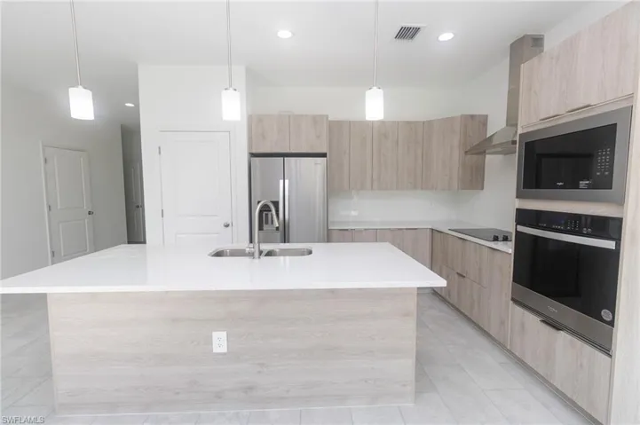 Kitchen with wall chimney range hood, modern cabinets, appliances with stainless steel finishes, and light brown cabinetry