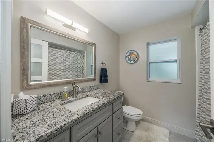 Vanity with granite countertop and integrated sink, framed mirror, and modern light fixture