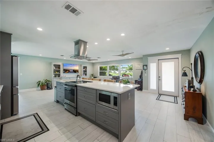 Spacious kitchen island with integrated microwave, stainless steel appliances, recessed lighting, and tile flooring