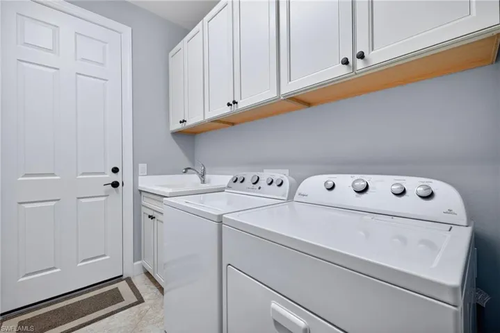 Dedicated laundry space featuring white shaker-style cabinetry with matte black hardware, a utility sink, and ample counter space