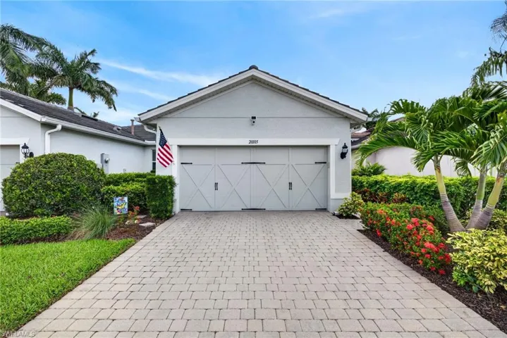 Property exterior featuring a paver driveway, an attached garage with decorative hardware, and lush landscaping