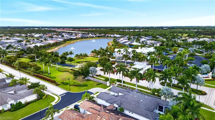 Expansive residential area featuring a central lake with multiple fountains, surrounded by lush green landscaping and numerous mature palm trees